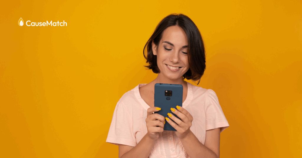 women looking down at her phone smiling in front of a bright orange background
